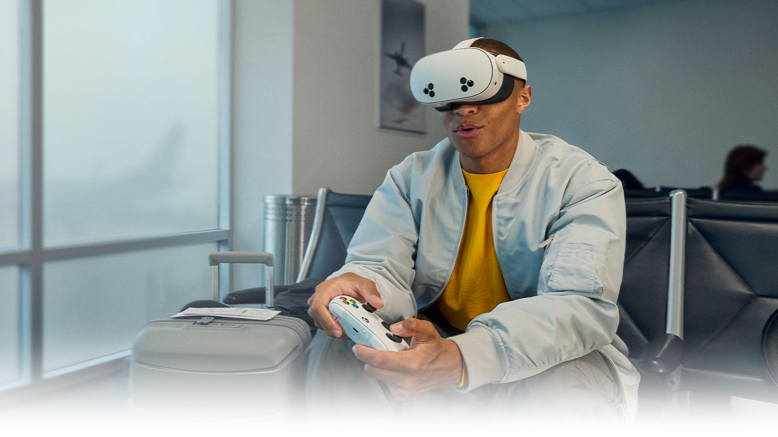 A person uses a VR headset and Xbox controller in the seating area of an airport